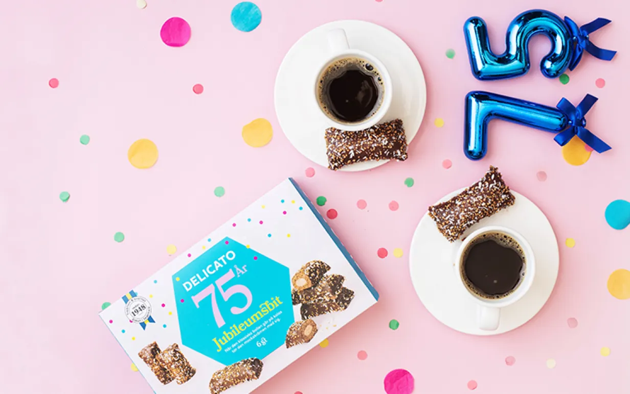 två koppar kaffe med en varsin kondisbit bredvid på ett ljusrosa bord