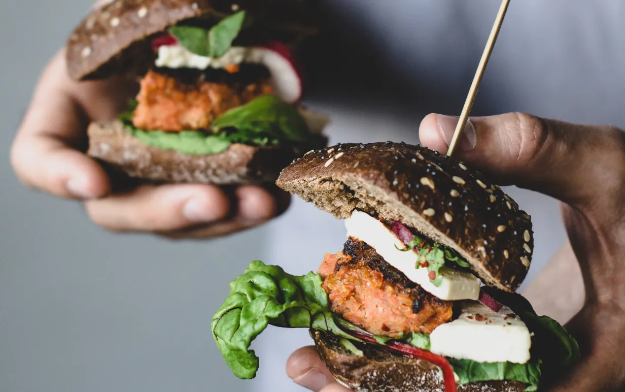 Ung man som håller två växtbaserade morotstofuburgare. Närbildvy, selektivt fokus