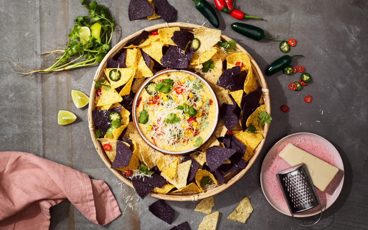 En skål med nachos och en liten skål med vegansk ostdipp mitt i den stora nachoskålen