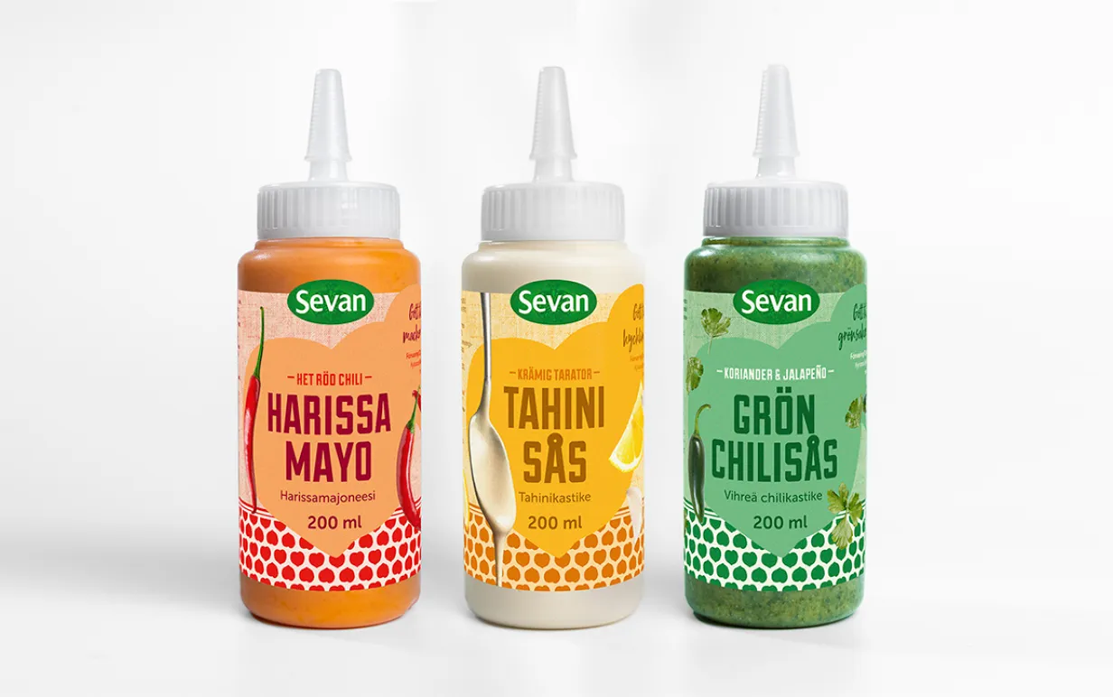 Tre flaskor med vegansk sås uppstaplade mot en vit bakgrund