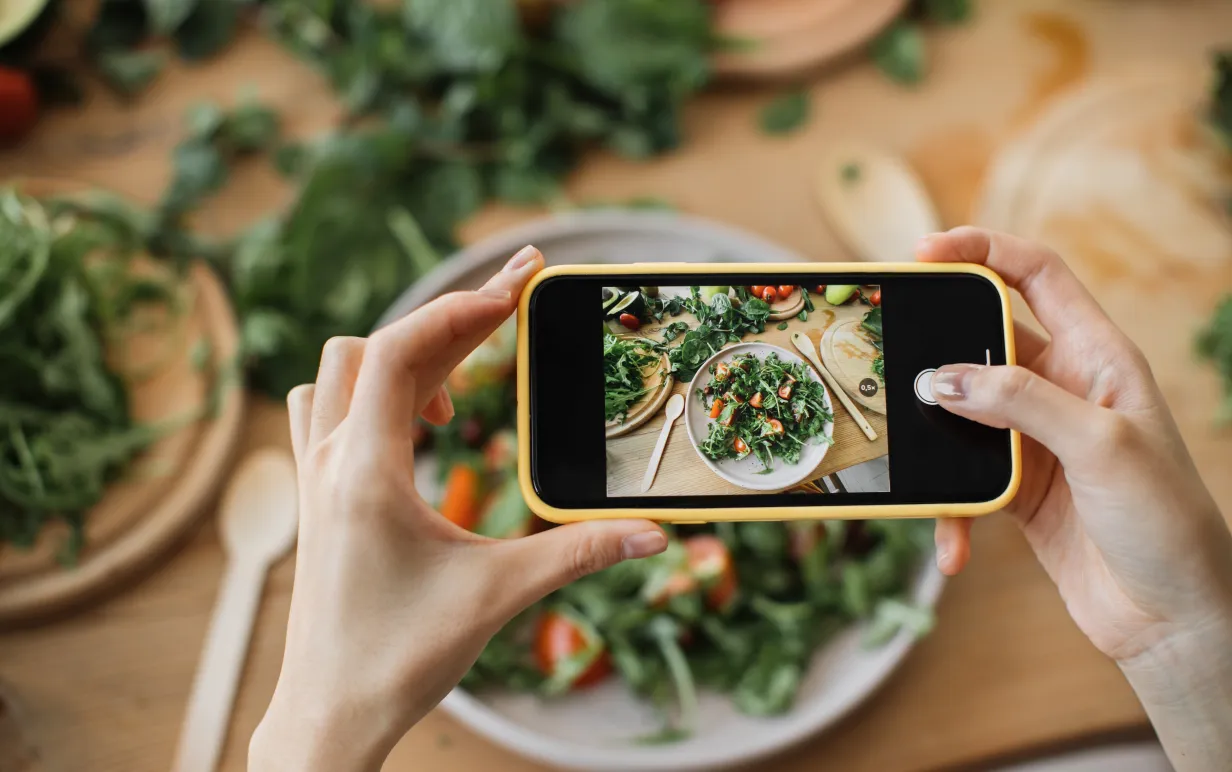 Kvinnahänder tar telefonfoto av matlunch eller middag. Grönsakssallad, avokado, ruccolatomater. Smartphonefotografering för sociala nätverk. Vegetarisk hälsosam mat.