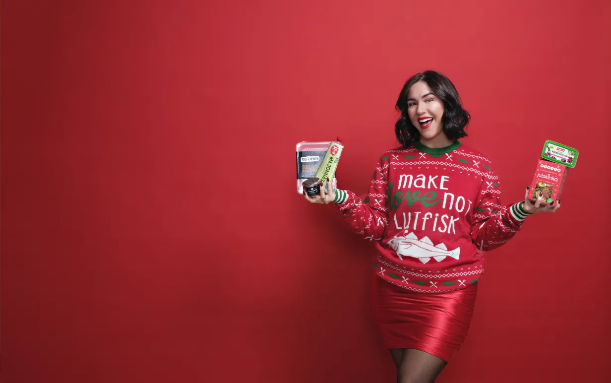 Mörkhårig tjej i röd jultröja mot en röd bakgrund hållandes i julmat