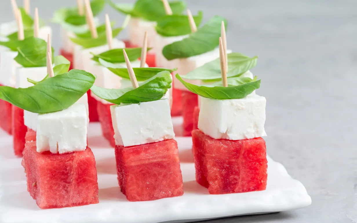 Snittar med melon, vegansk fetaost och basilika på ett vitt fat.