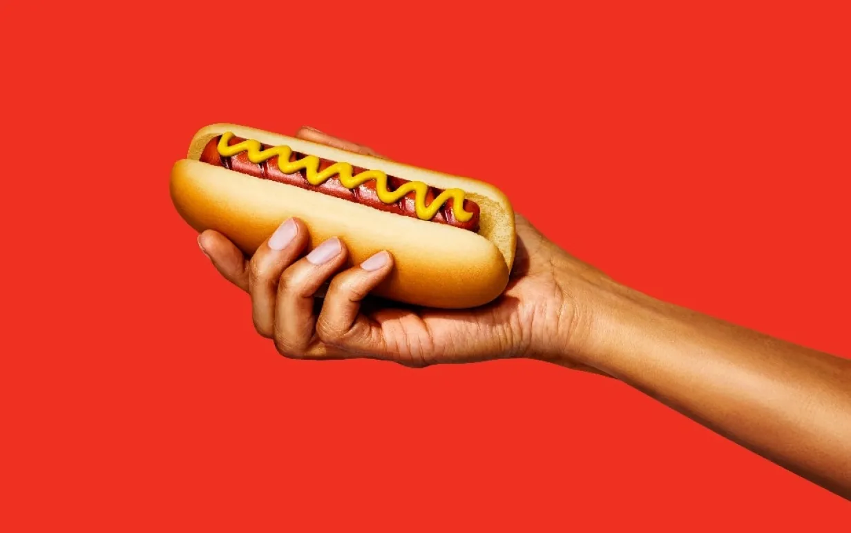 En hand som håller upp en växtbaserad korv mot en röd bakgrund