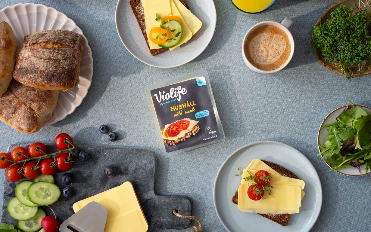 ett frukostbord med bröd, tomater, gurka, grönt och växtbaserad ost