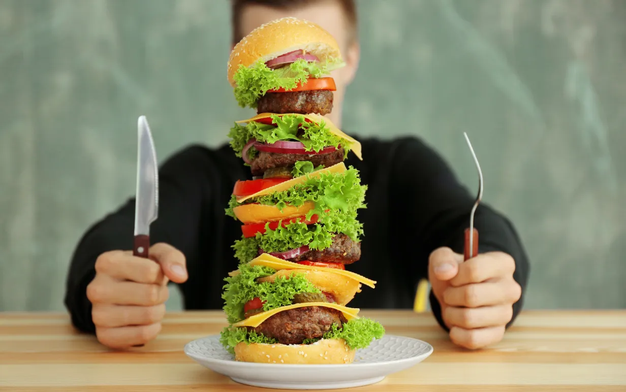 Man äter en stor hamburgare vid ett bord