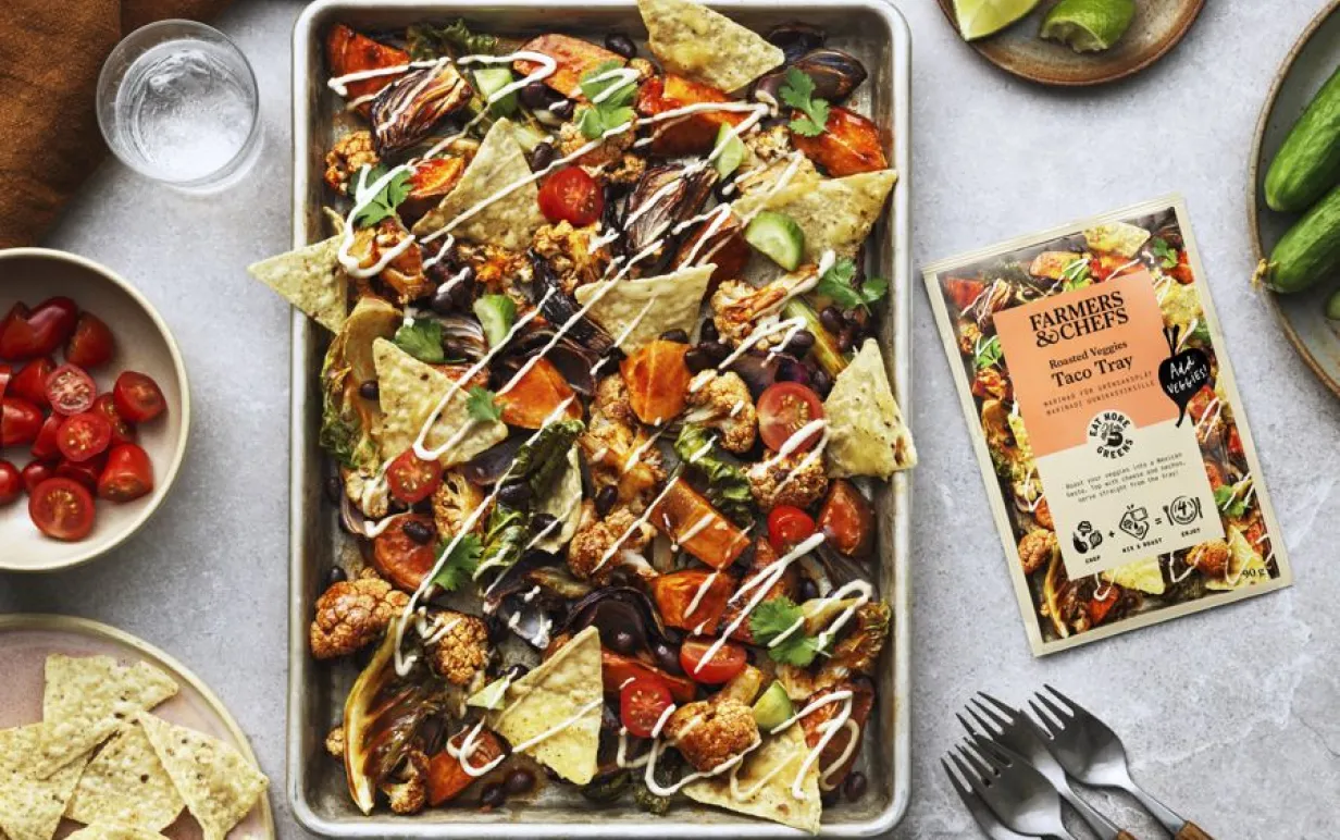 En plåt med dressade nachos på ett ljust bord med tillbehör på sidorna