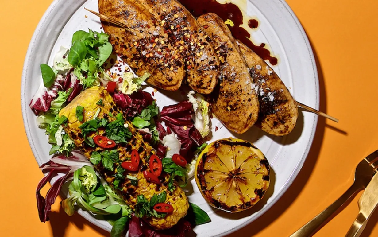 Vegofiléer med majskolv och grönsaker på en tallrik, på ett oranget bord.