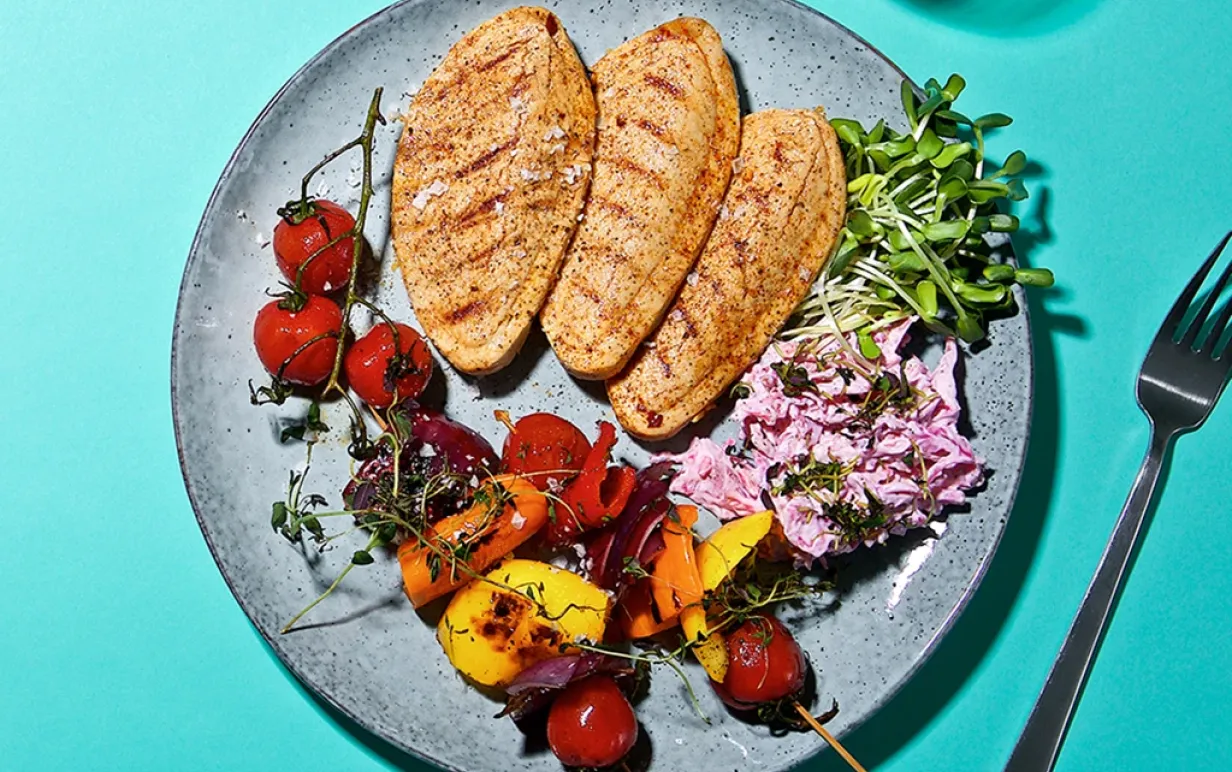 tre vegofiléer med grönsaksspett och coleslaw på en tallrik, på ett turkost bord