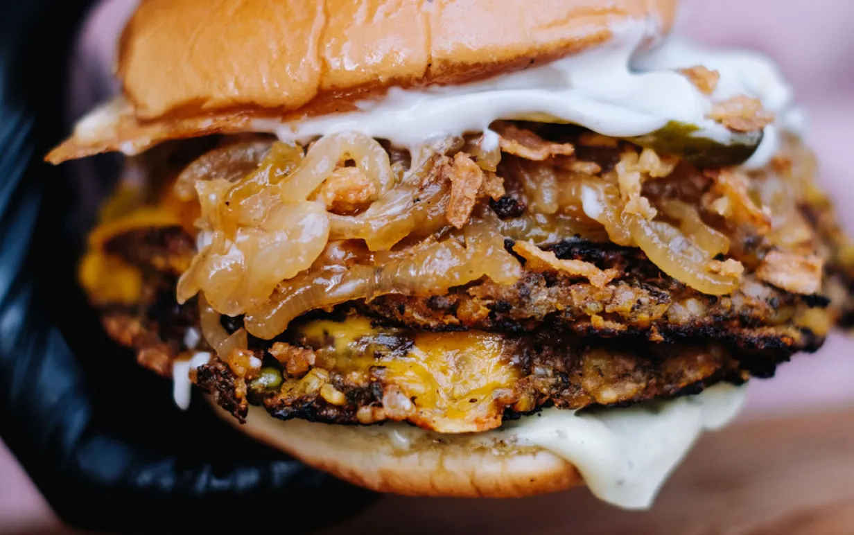 En hand med svarta handskar som håller i en växtbaserad burgare