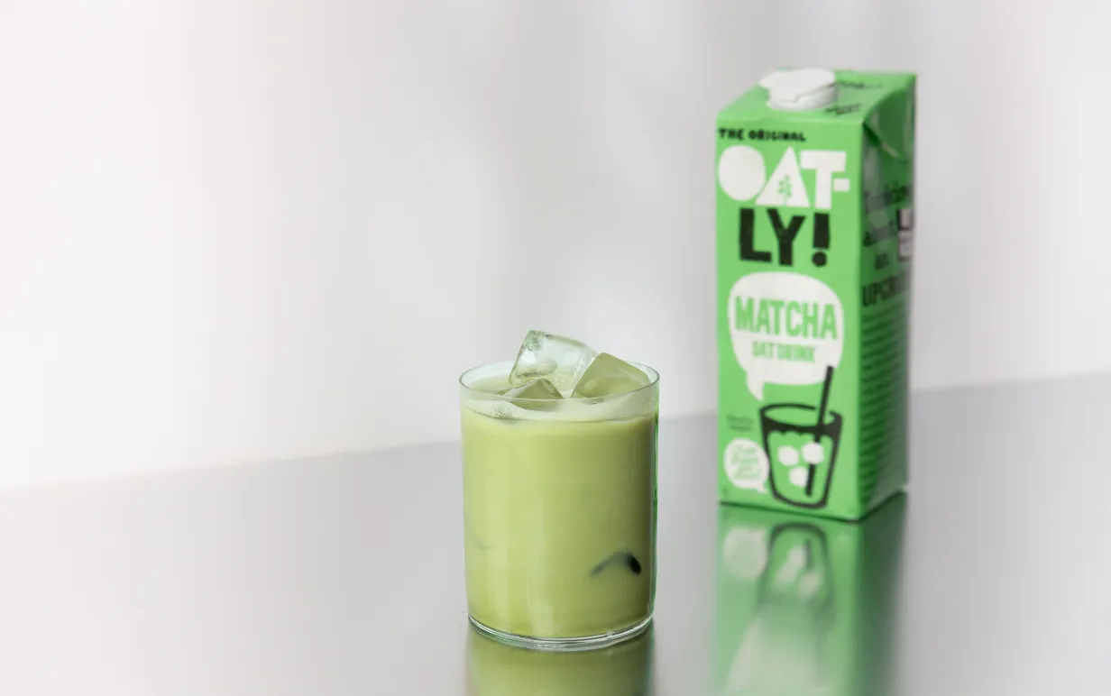 Ett glas med matcha latte och en tetra med färdigblandad matcha latte bredvid på ett silverbord.