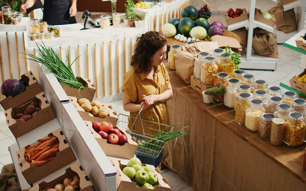 Zero waste store customer roaming around aisles adding healthy natural pantry staples to shopping basket, aerial drone shot. Local grocery shop client buying preservatives free bulk food items