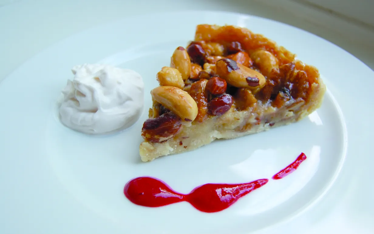 Vegansk nötpaj med vaniljgrädde och hallonsås på en vit tallrik