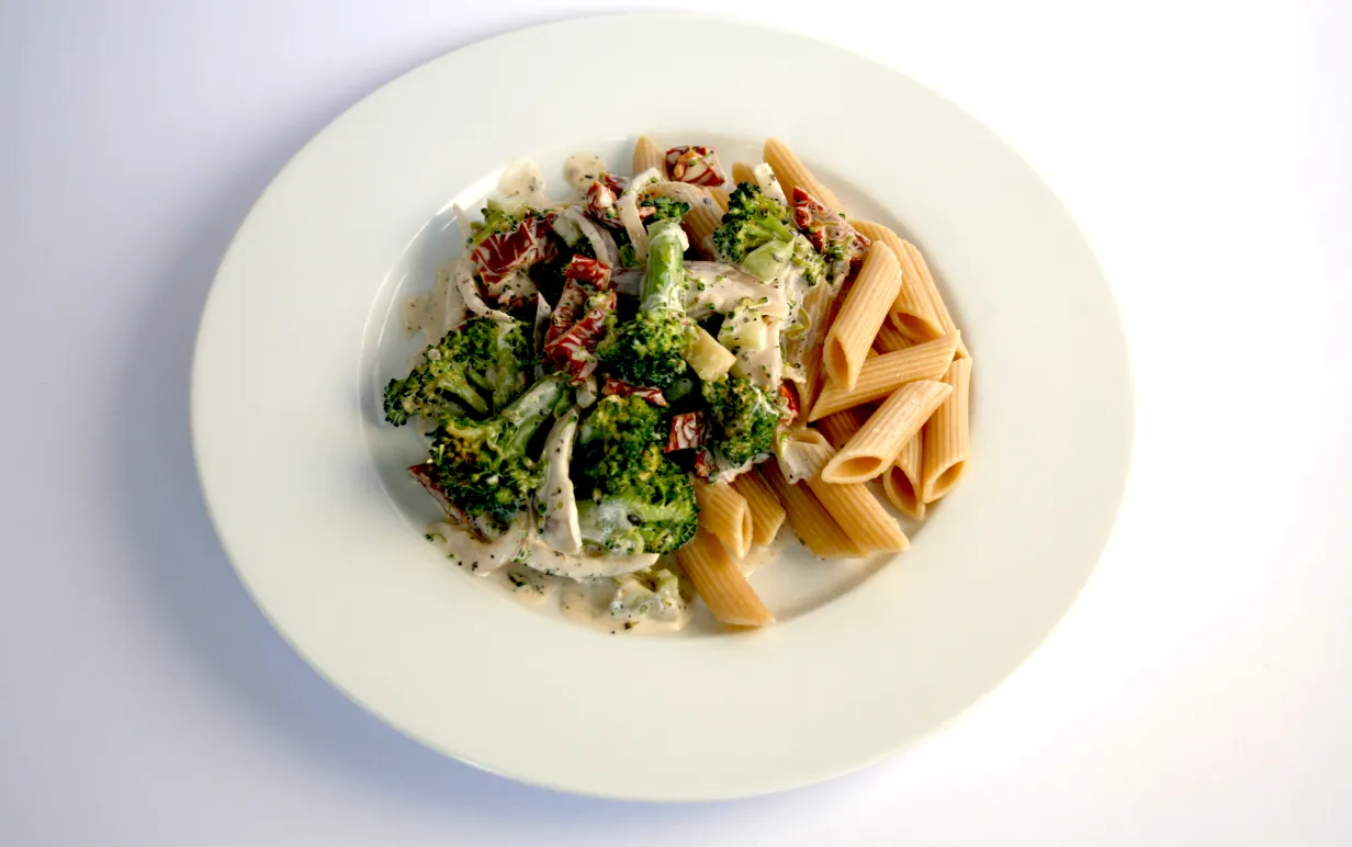 Pasta med broccoli och soltorkade tomater på en vit tallrik
