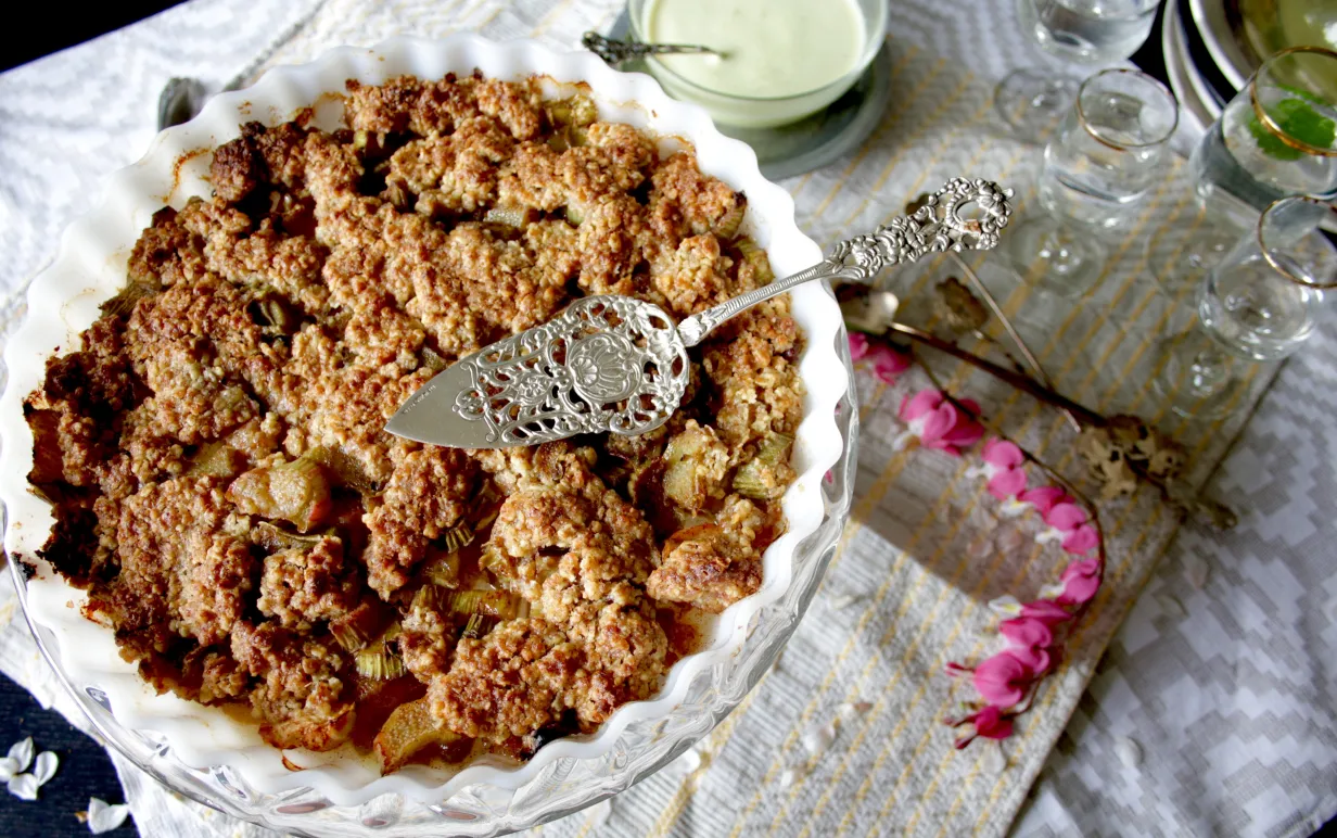 Rabarberpaj i en vit form på ett vit duk, bredvid ligger en rosa blomma.