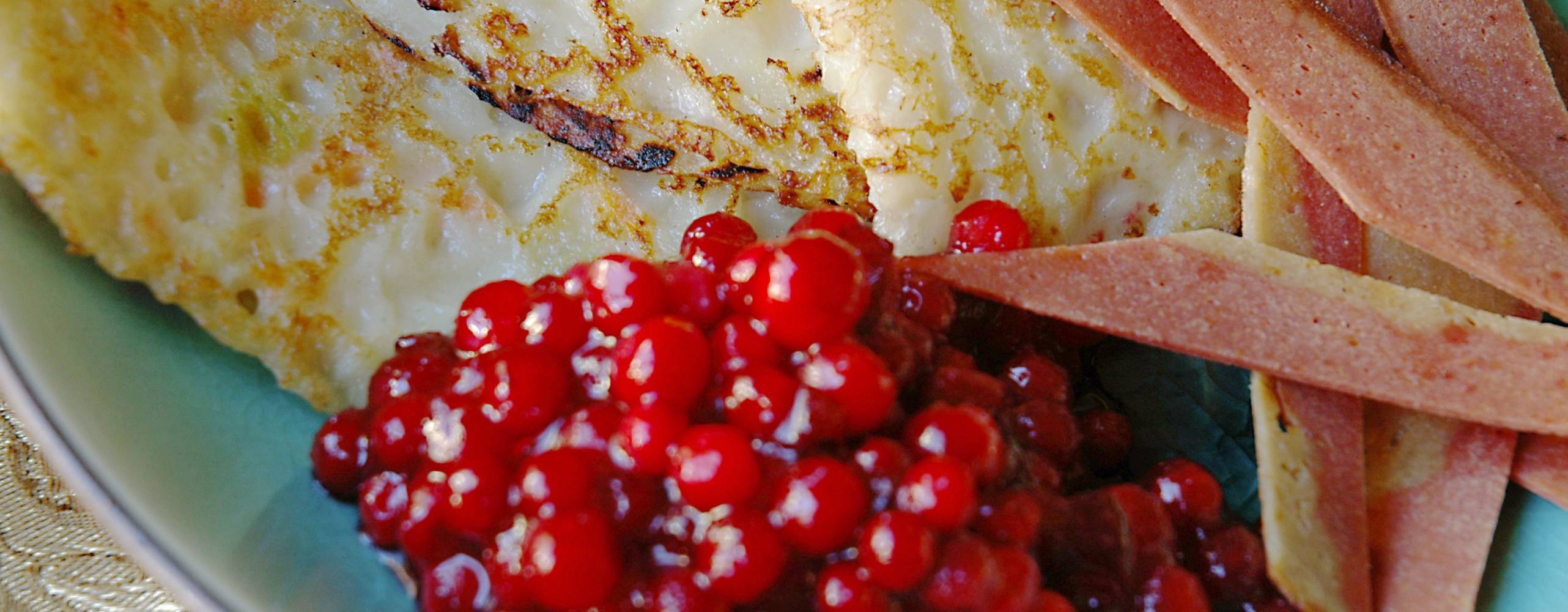 Raggmunkar med stekt bacon och rårörda lingon på ett blått fat.