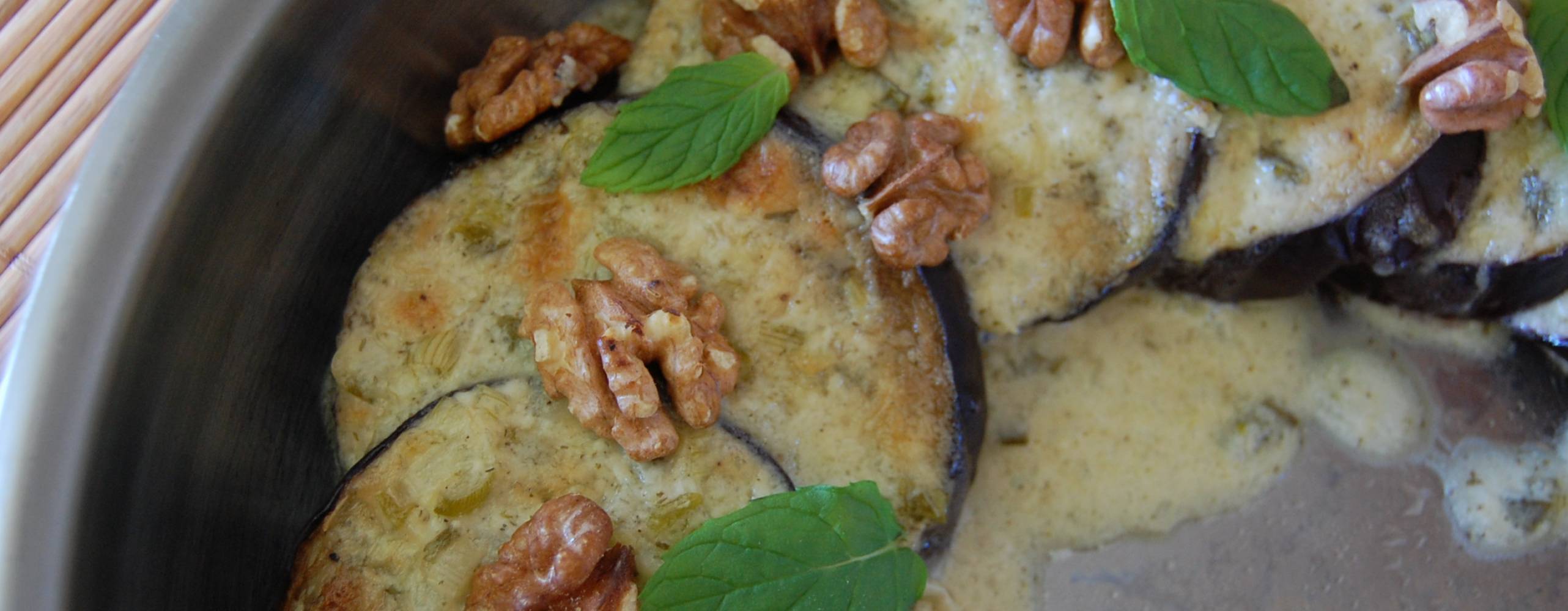 Ostkrämsgratinerade auberginer i en grå form, dekorerade med mynta och valnötter