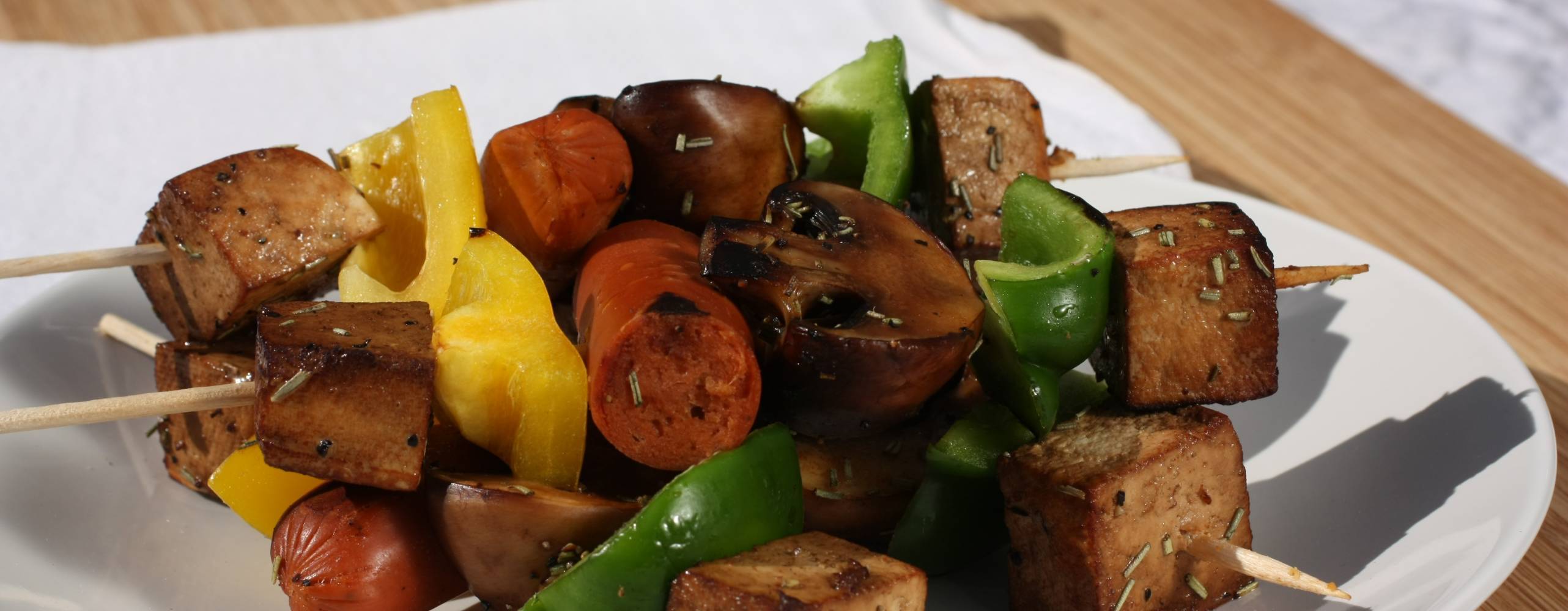 Grillspett med svamp, paprika, tofu och kryddig korv Grillspett med svamp, paprika, tofu och kryddig korv på en vit tallrik