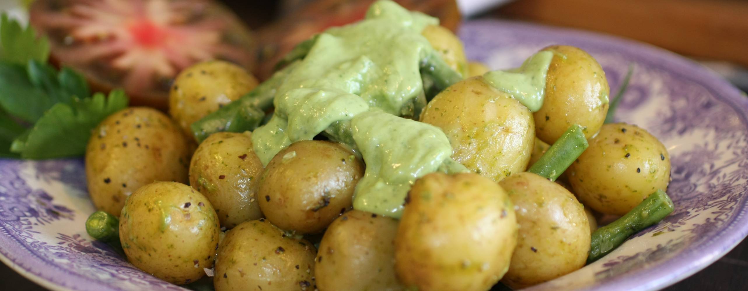 Potatissallad med grön dressing och haricoverts på ett blåvitt fat.
