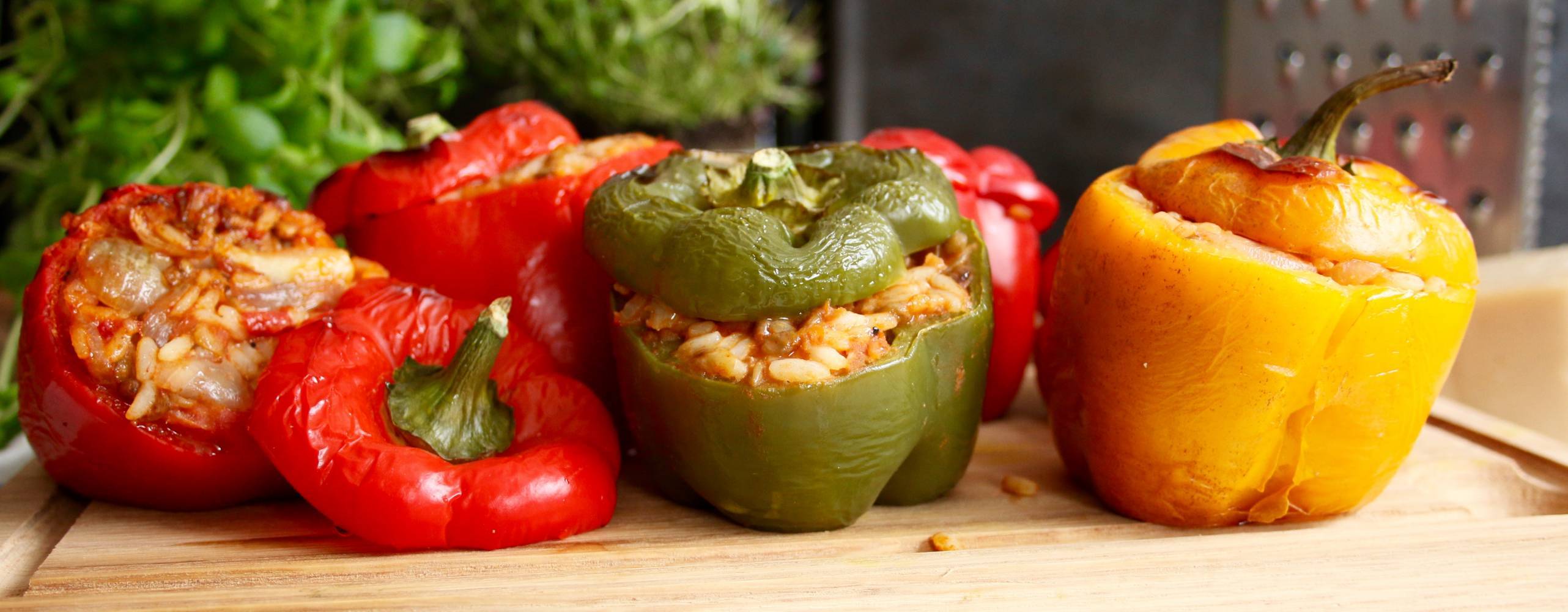 En röd, en grön och en gul paprika med fyllning på en skärbräda
