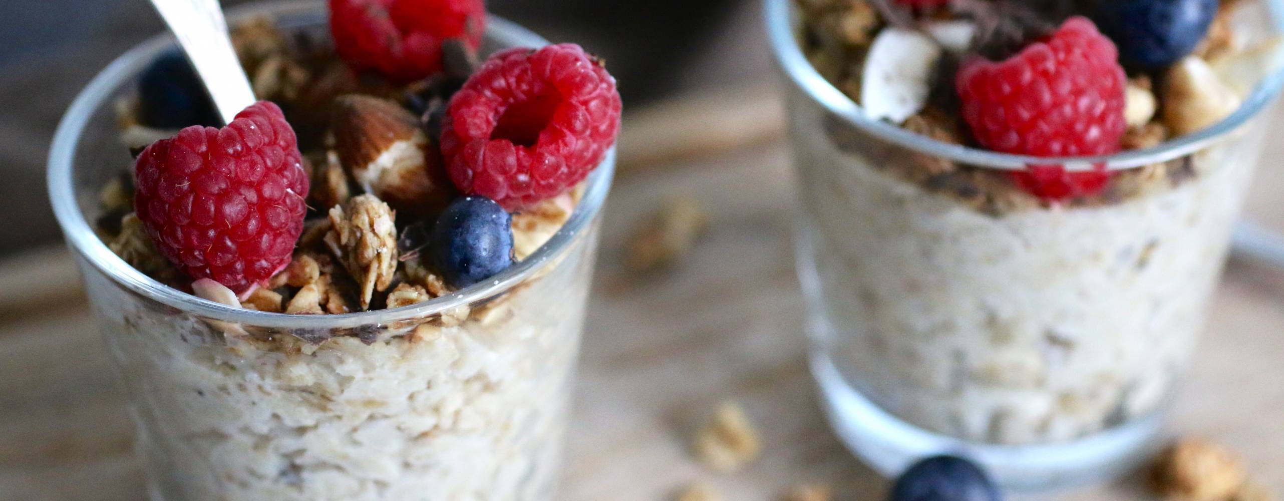 Två glas med overnight oats toppade med hallon och blåbär.