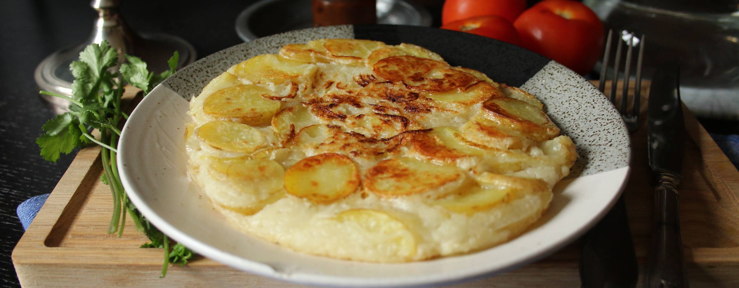 en vit tallrik med spansk potatisomelett på en skärbräda, bredvid tallriken ligger några tomater