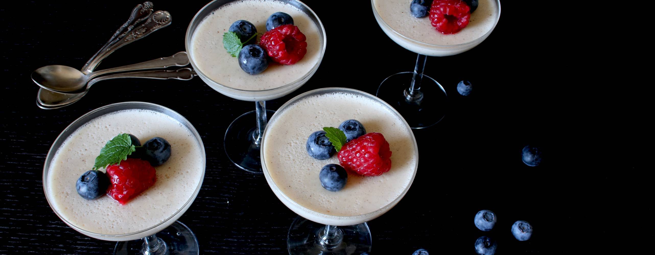 Fyra glas med pannacotta, dekorerad med hallon och blåbär.