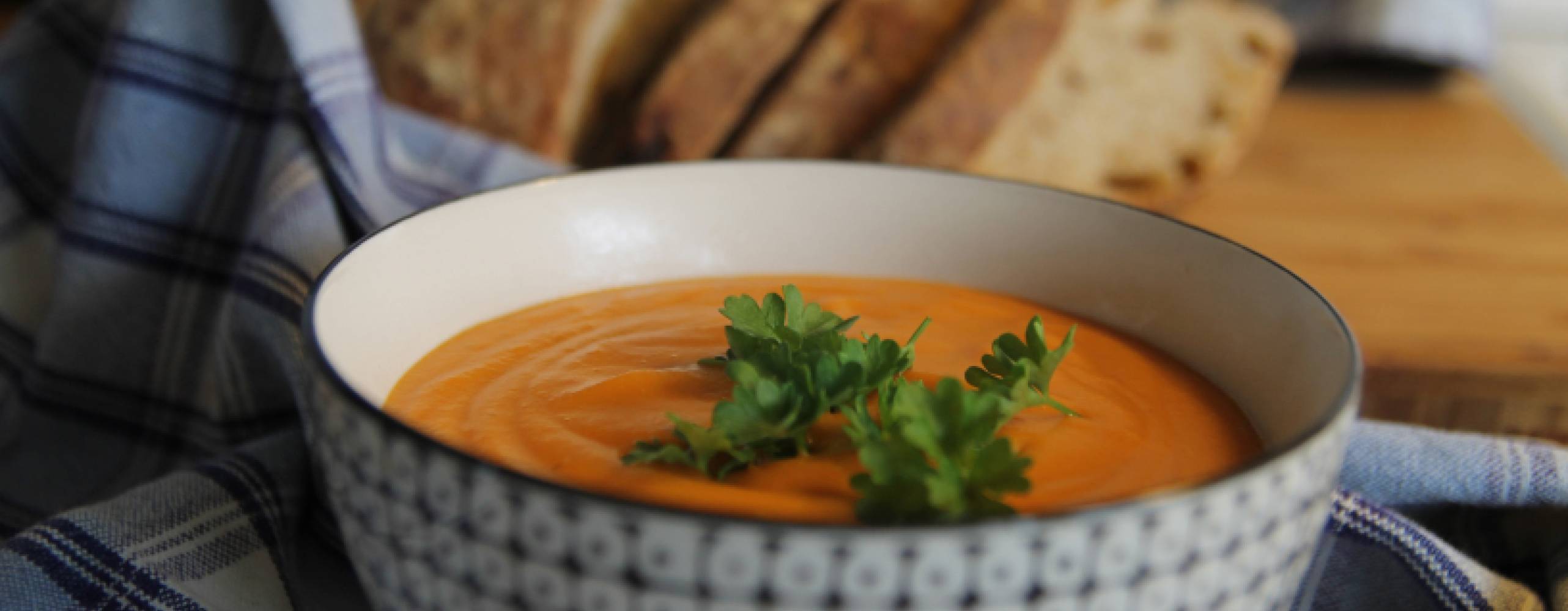 Sötpotatissoppa Sötpotatissoppa i en skål på en rutig handduk på ett bord. Det ligger bröd bredvid handduken.