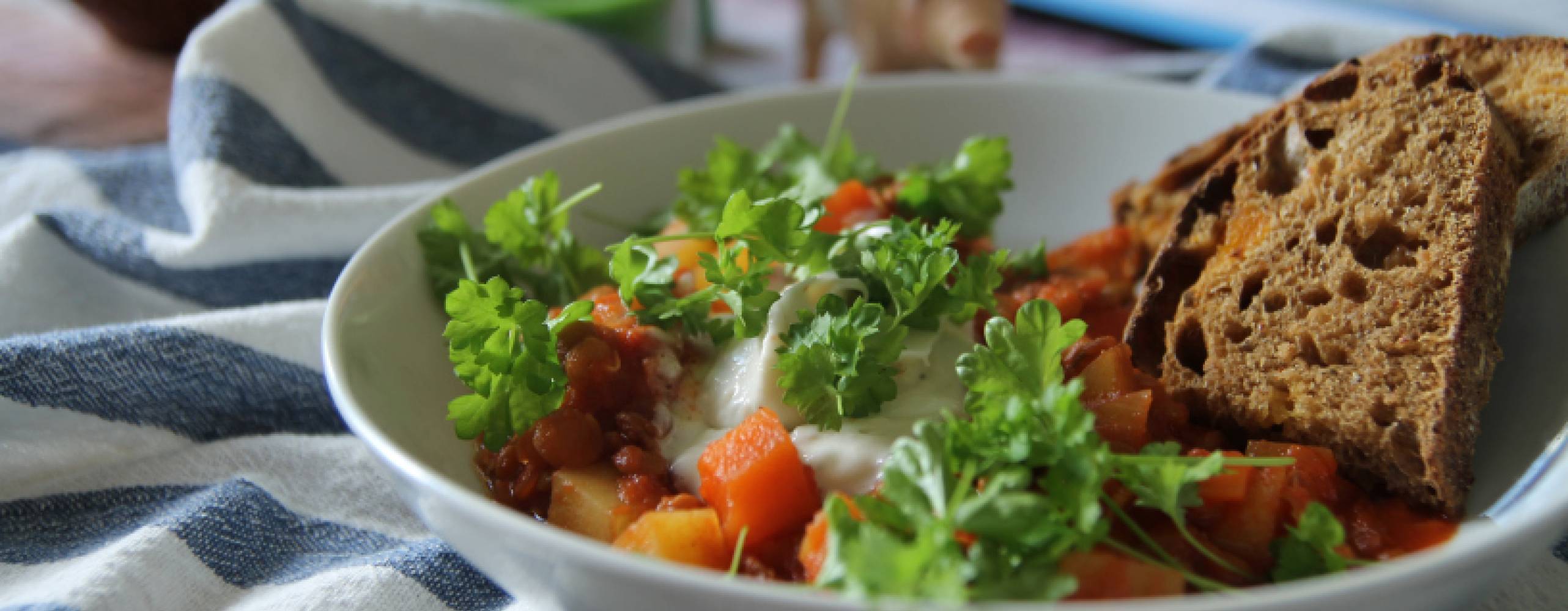 Linsgulasch med persilja i en vit skål står på ett bord med rutig duk