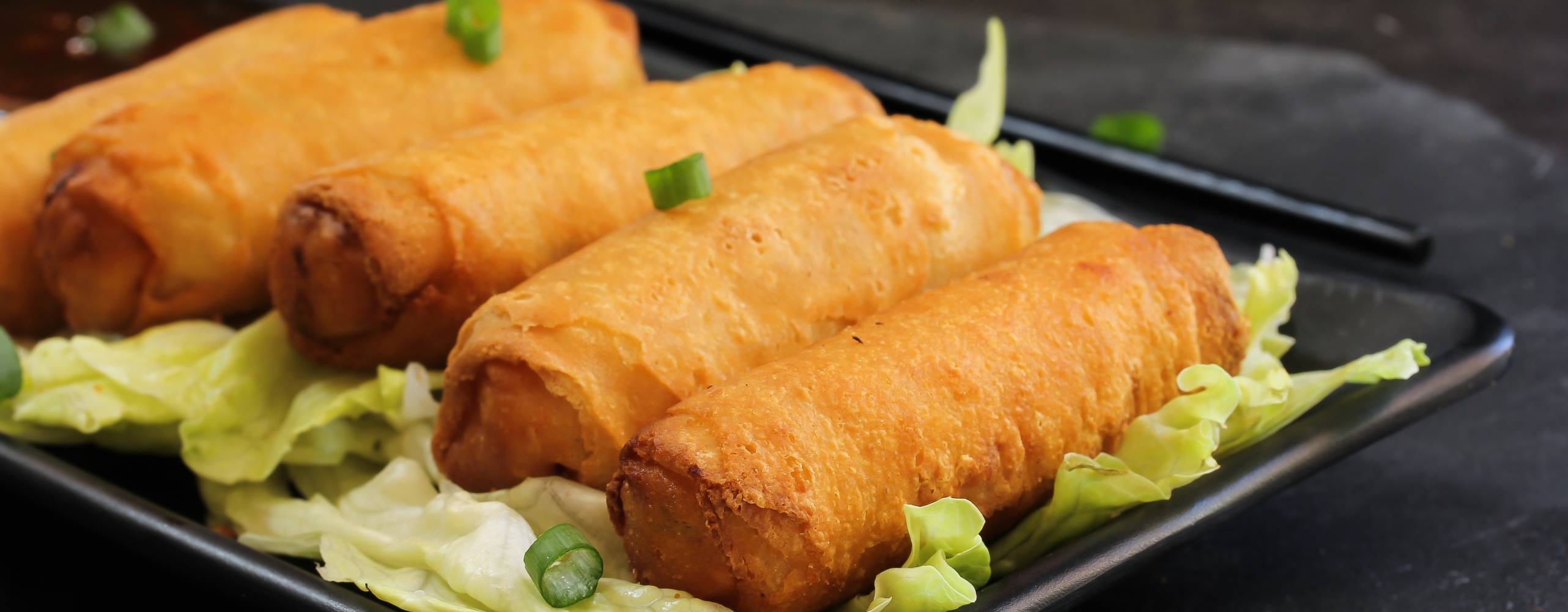 Minivårrullar med tofu Fem vårrullar på en svart tallrik.