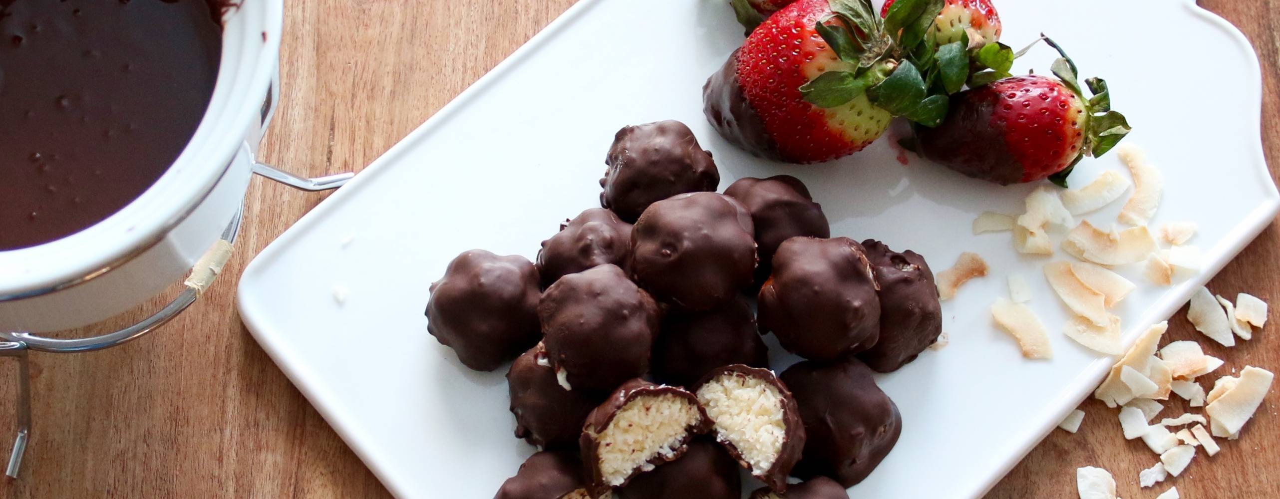 Smarriga chokladbitar med kokos Chokladbitar med kokosfyllning på en vit skärbräda, bredvid ligger några jordgubbar och kokosbitar