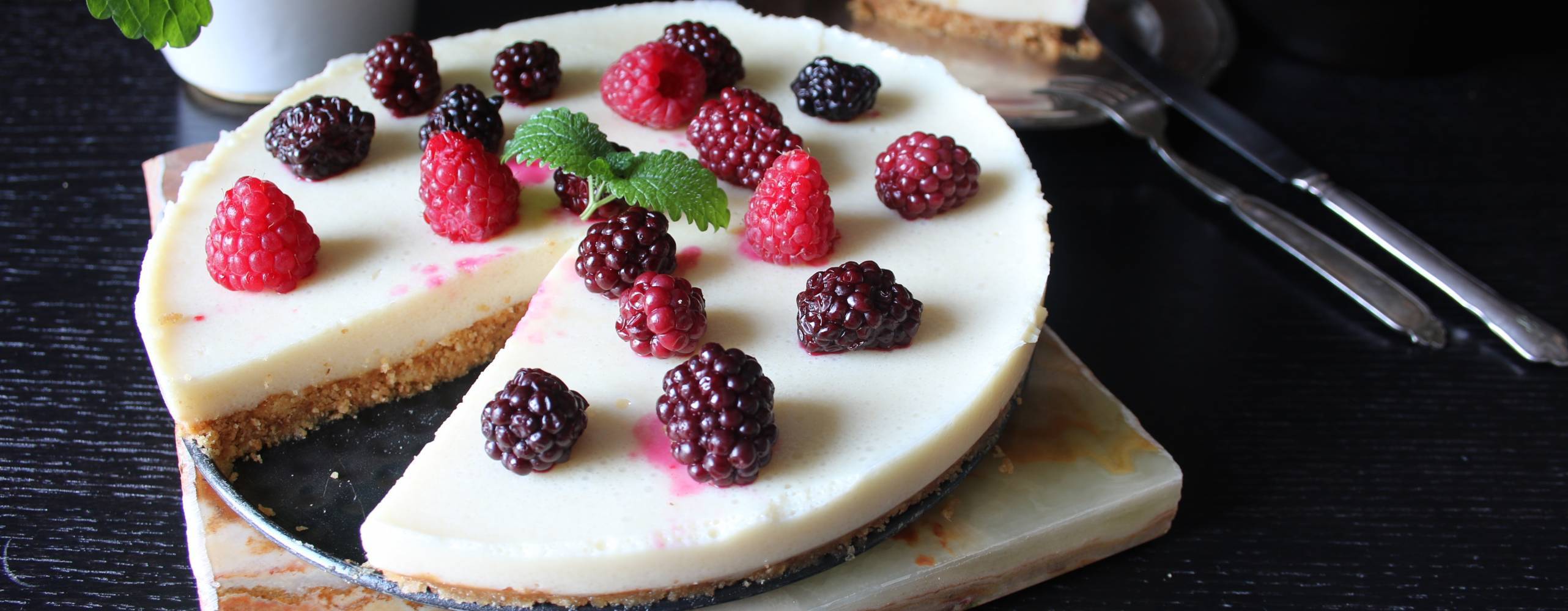 Cheesecake med citronfyllning dekorerad med hallon och björnbär på ett mörkt bord