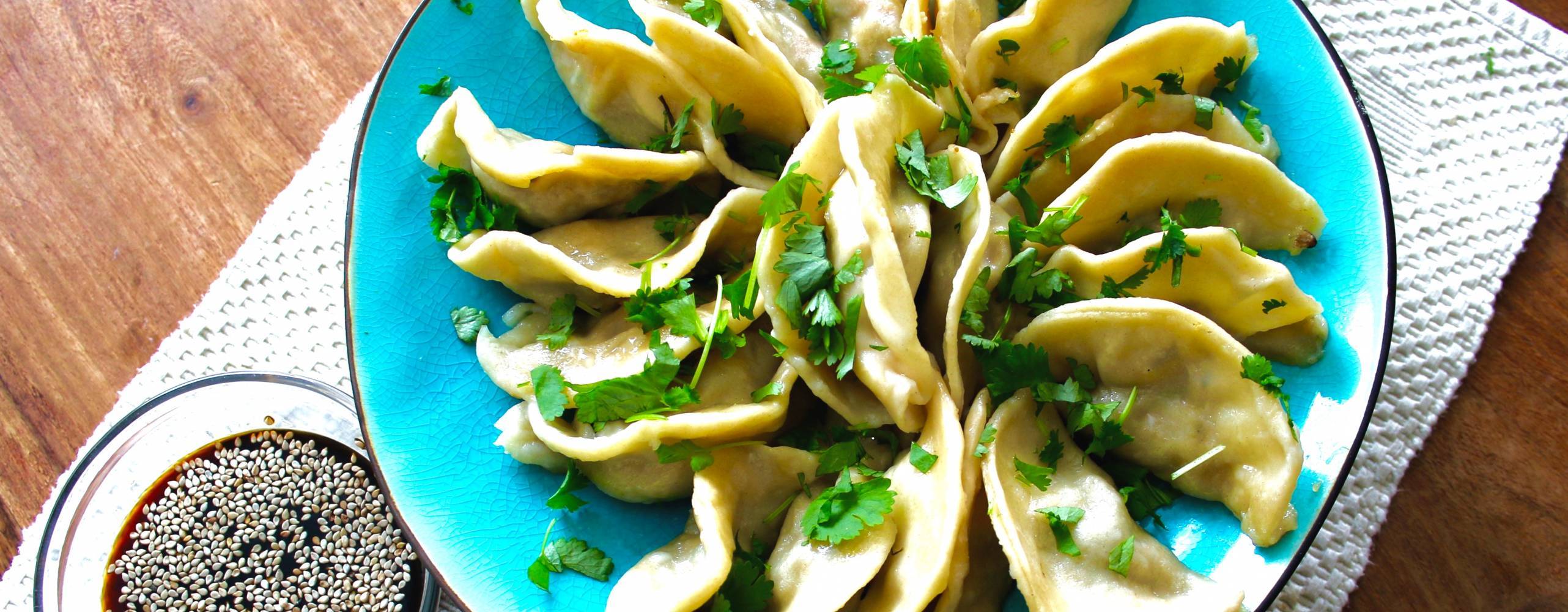 Veganska dumplings på ett blått fat. Bredvid står en skål med japansk soya.