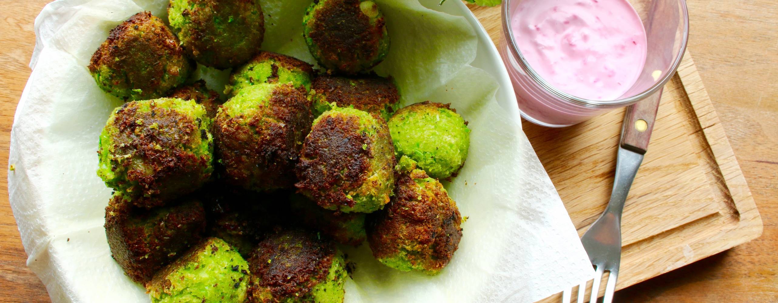 ärtbollar i en vit skål på en skärbräda, bredvid står en skål med rödbetssås