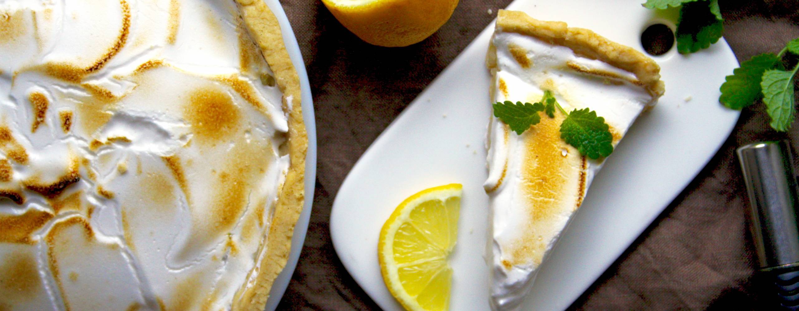 Syrlig citronpaj med vegansk maräng En citronpaj med marängtäcke, bredvid pajen ligger några delade citroner