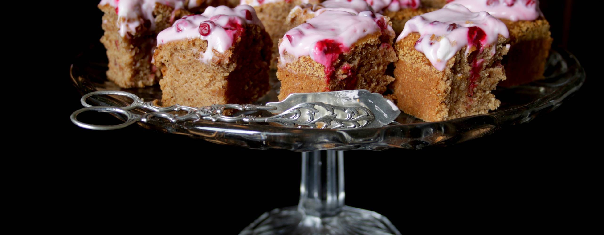 Mjuk pepparkaka med lingonfrosting Bitar av mjuk pepparkaka med lingonfrosting på ett kakafat av glas.