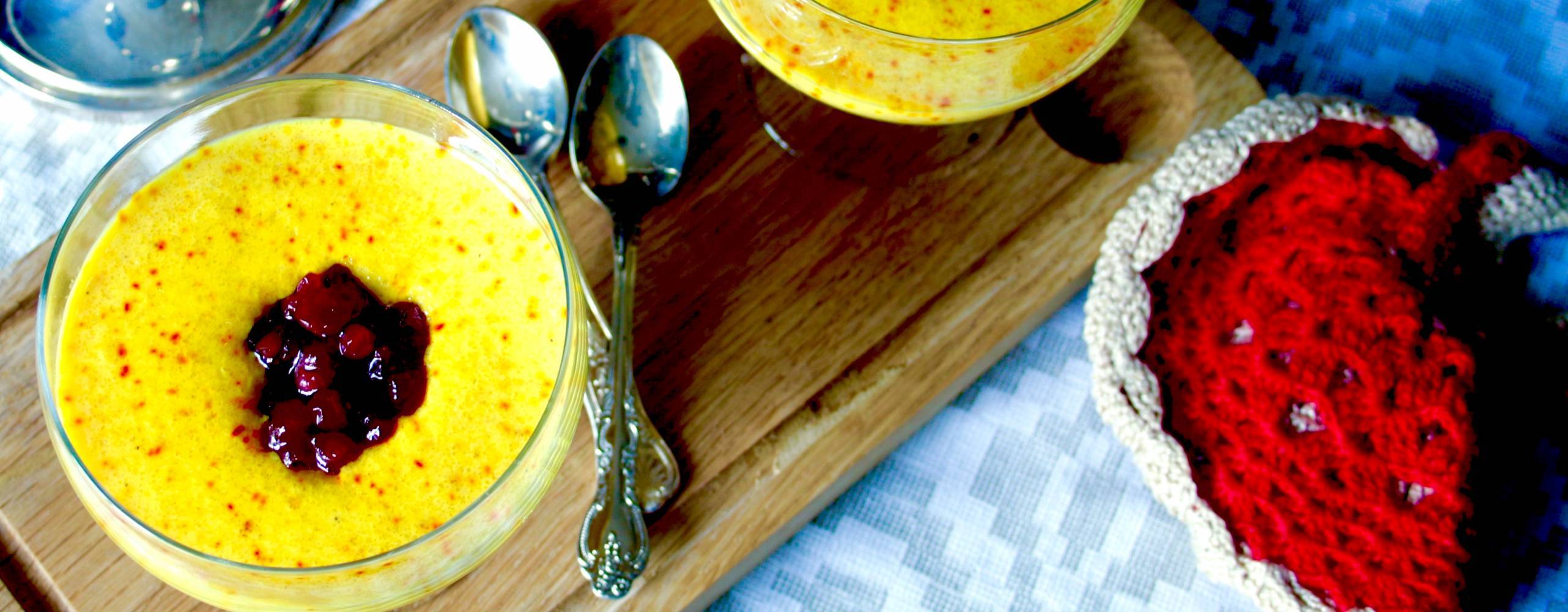 Två bägare med mannagrynsgröt med smak av saffran, toppade med lingonsylt, på en träskärbräda.