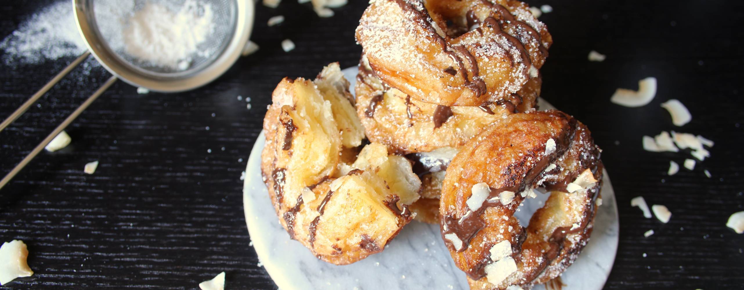 Cronuts med choklad och kokosflarn på ett vitt fat på ett mörkt bord