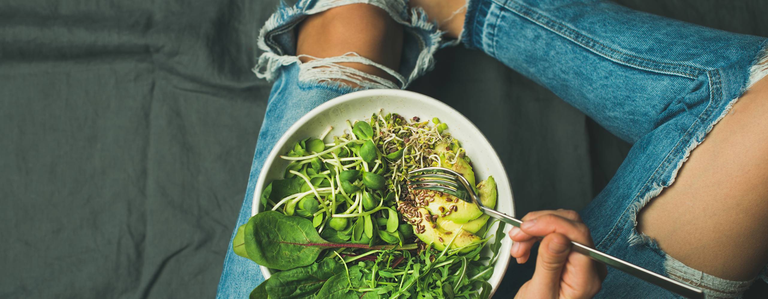 Skål med groddar, avokado och spenat på en persons ben