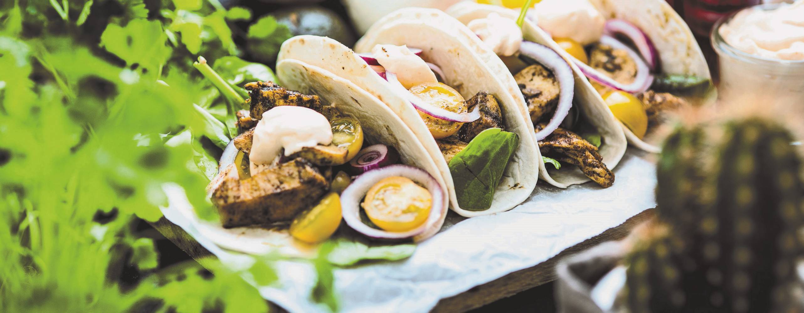 Jamaican jerked taco Fyra stycken tacos ligger på en vit handduk, i förgrunden syns gröna blad