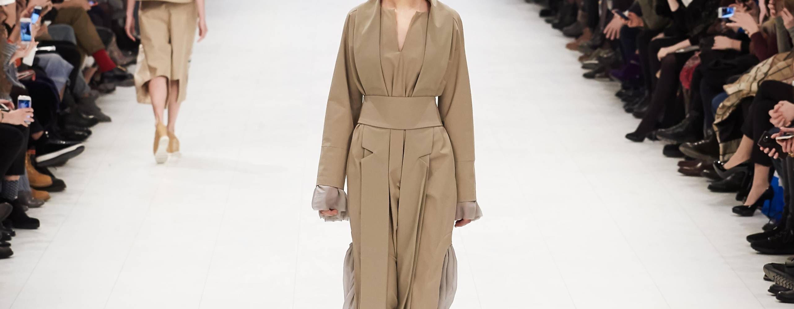 Shutterstock Webum En catwalk med en person i mitten med en trenchcoat och åskådare på varje sida