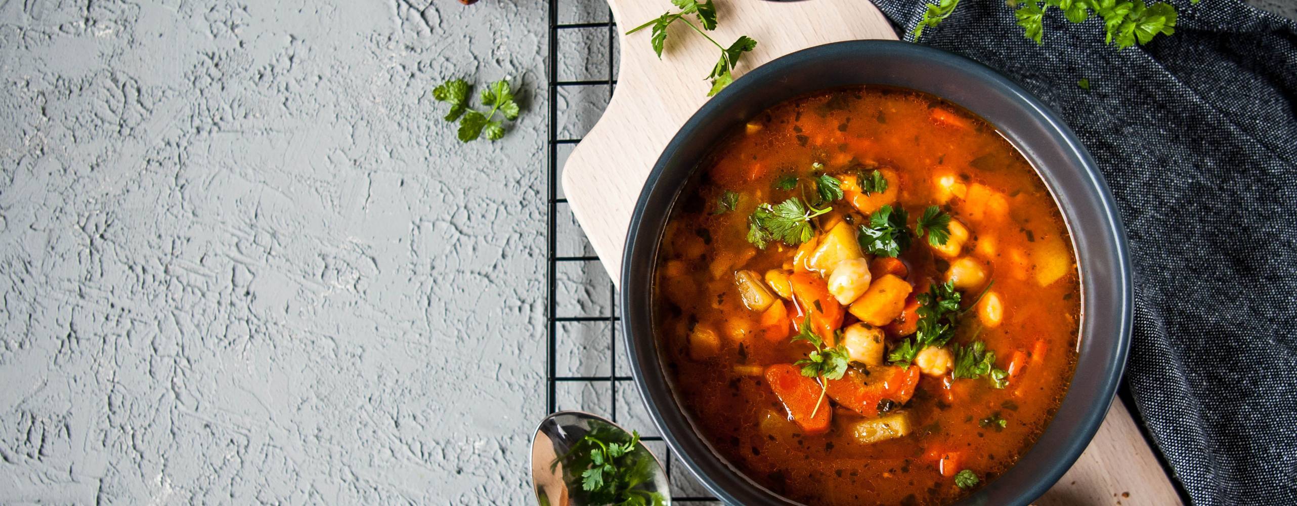 Bild på en gryta som står på en skärbräda i trä med kryddor omkring