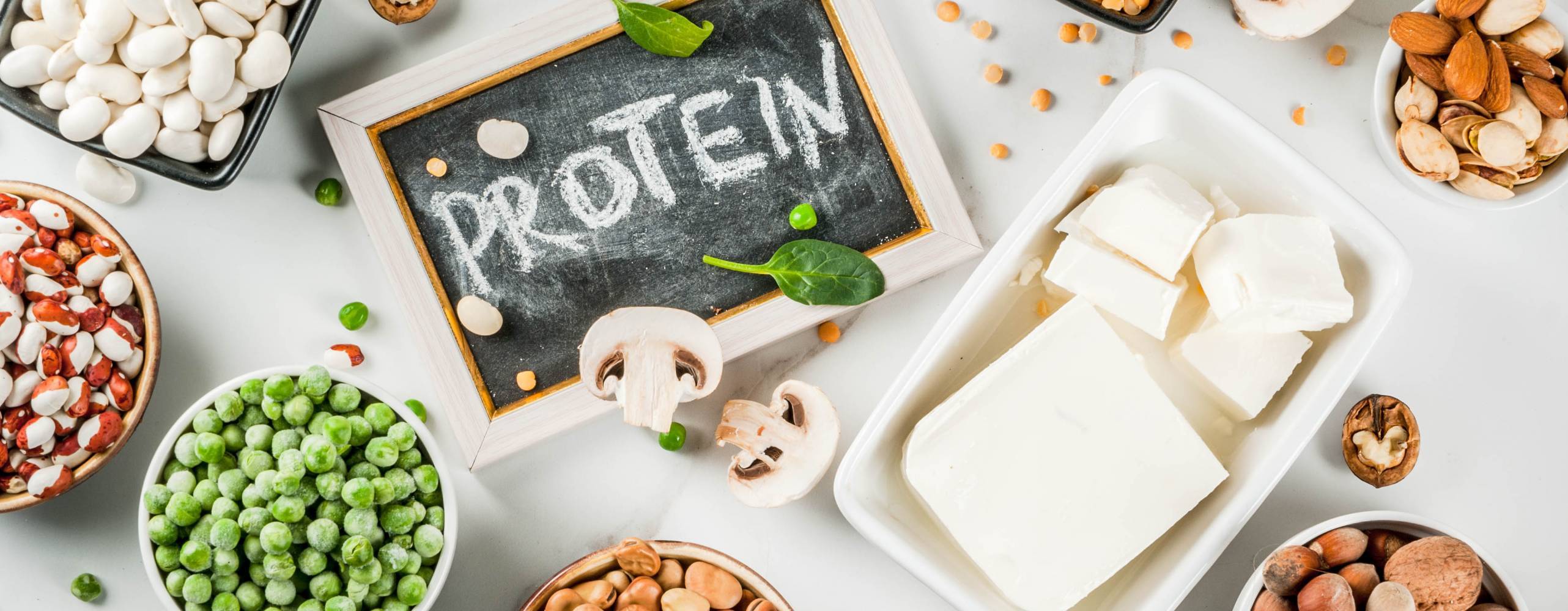 Shutterstock - Rimma Bondarenko Flera bönor, tofu och nötter på ett bord och en krittavla med ordet: Protein