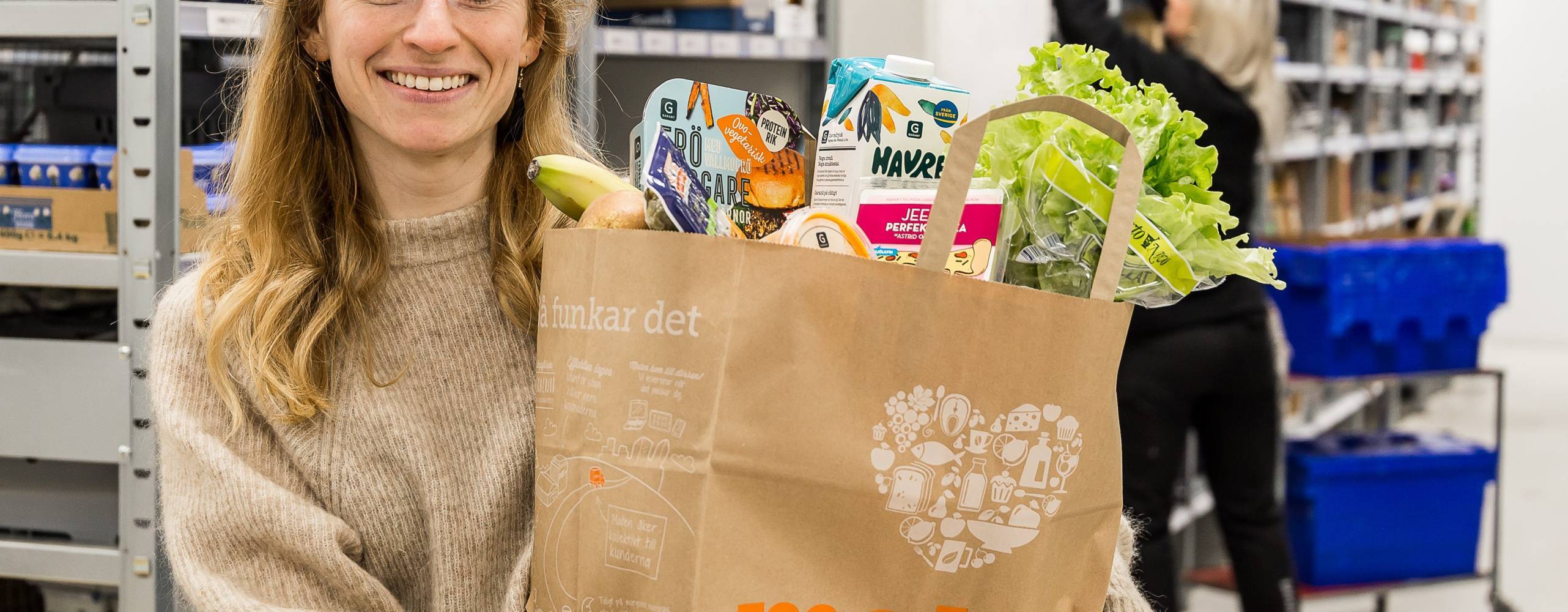 Person står i en lagerlokal med en matkasse fylld med veganska produkter