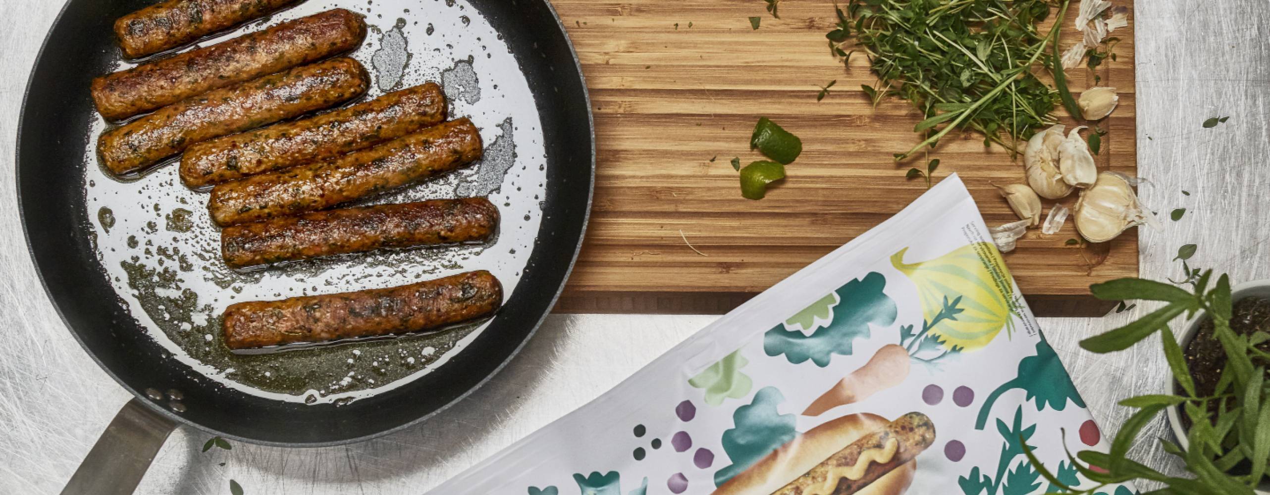 Händer hackar gräslök och det ligger ett par veganska korvar på en panna intill