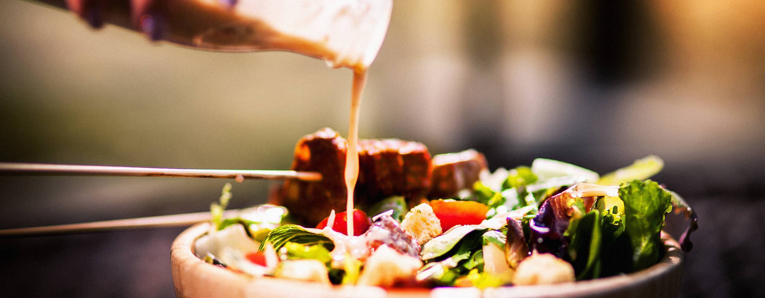 Vegansk caesarsallad med tempeh och en hand som häller på dressing