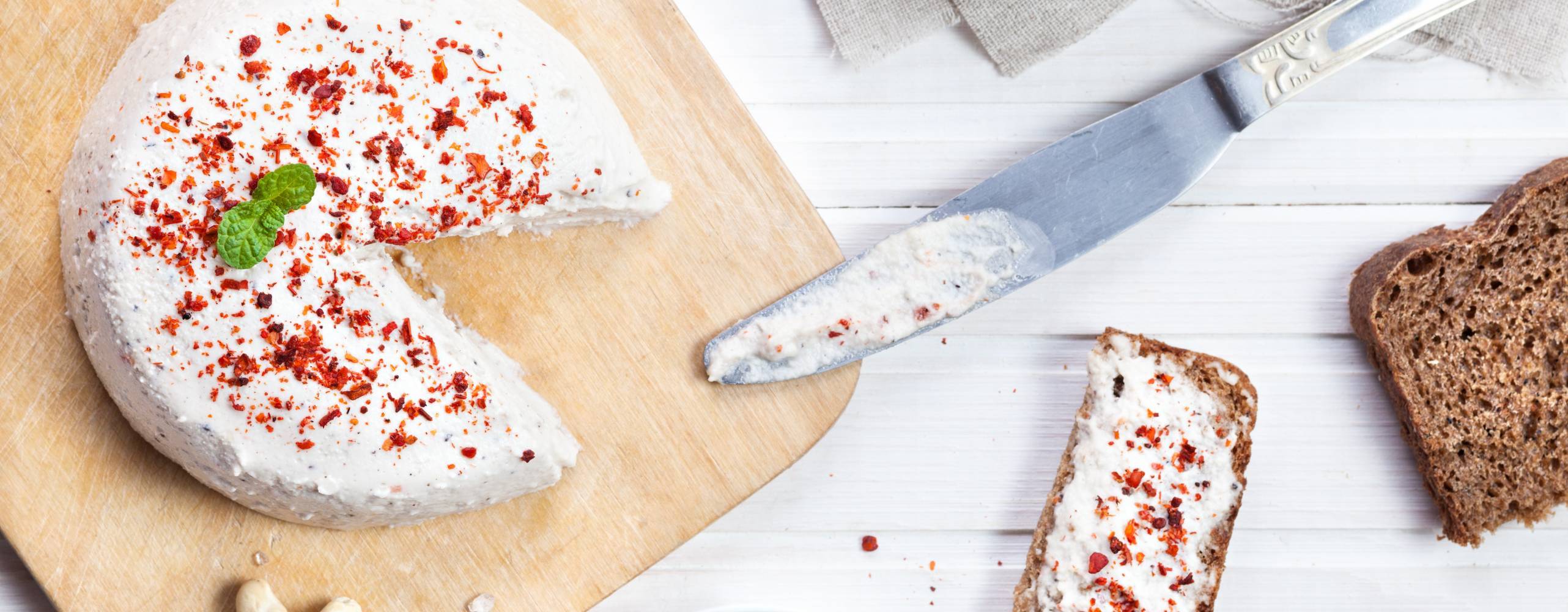 Egengjord cashewost Vegansk cashewost toppad med chiliflingor på en skärbräda.