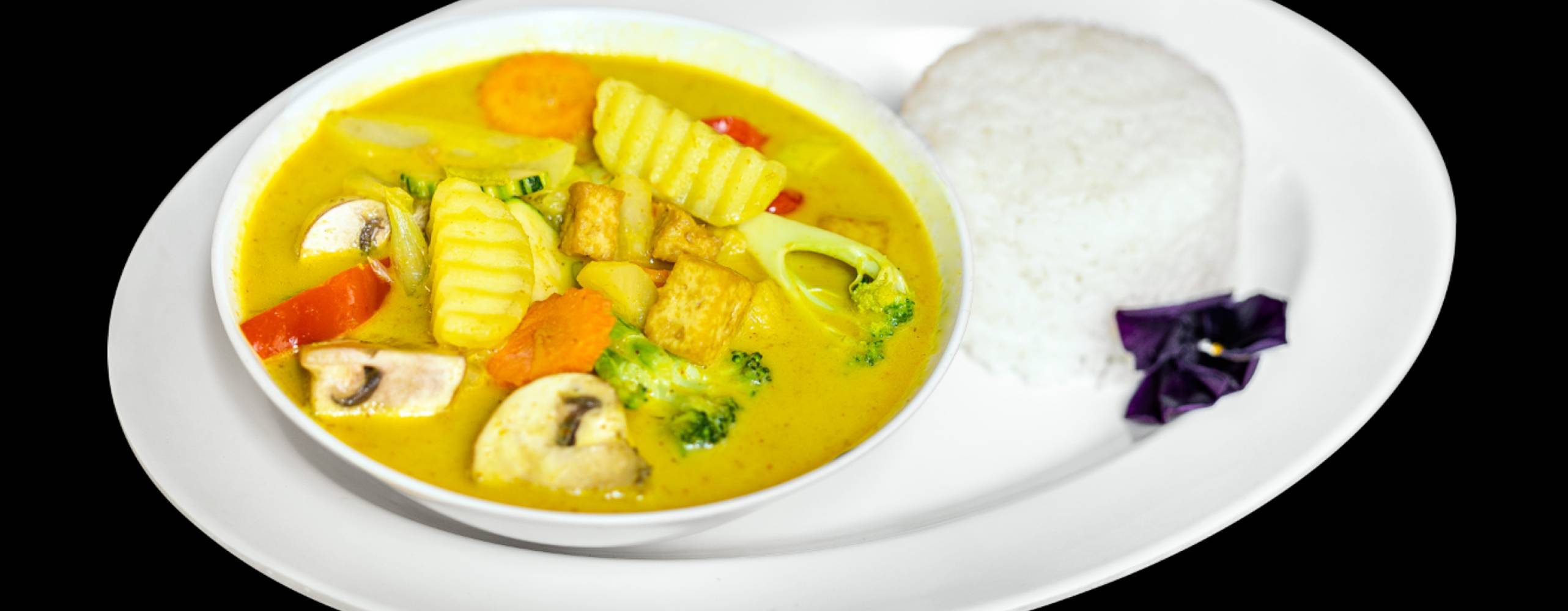 Foto: webbtech.nu Mae Thai Stockholms veganska gula curry med tofu, grönsaker och ris på en vit tallrik med svart bakgrund.