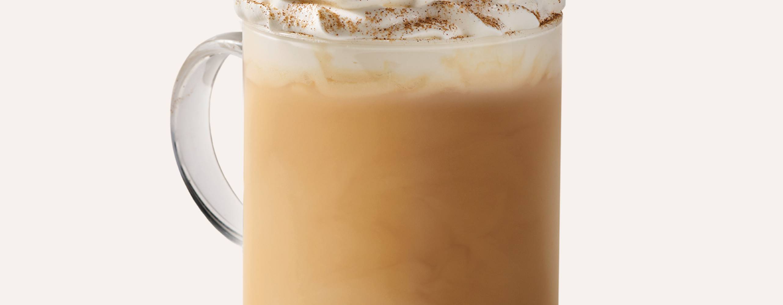 En glaskopp med pumpkin spice latte i och grädde toppad med kanel på toppen mot en vit bakgrund.