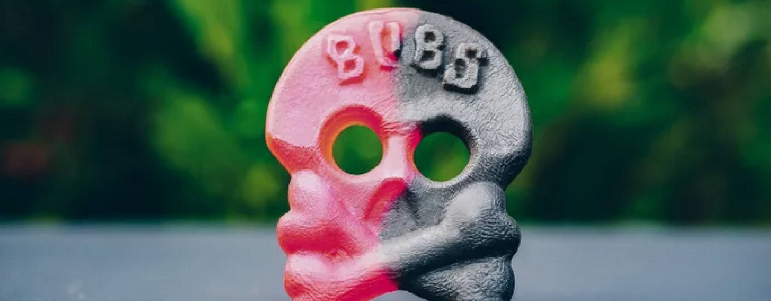 Hallonlakritsskallen, röd ena halvan svart andra halvan, står BUBS i pannan, står på ett svart golv mot en grön bakgrund